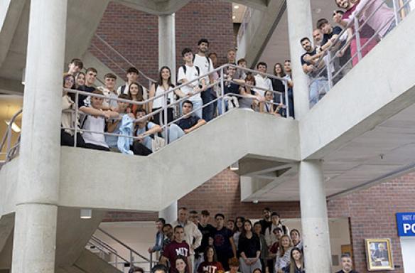 Portrait of dozens of 2024 visitng students standing at the railing of several stories in the lobby of CCTR